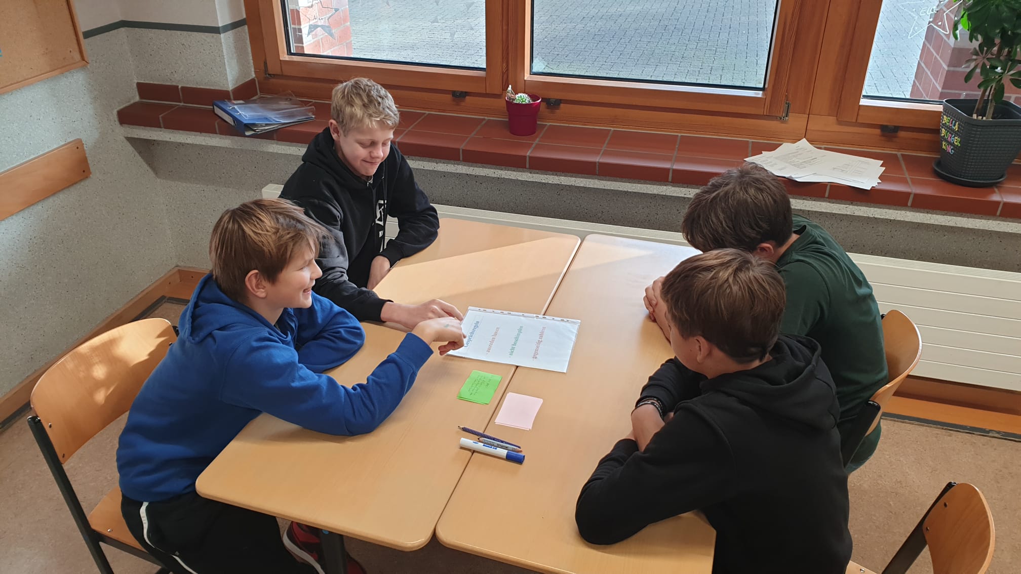 Streitschlichter und Streitende im Rollenspiel-Training sitzen am Tisch und klären die Gesprächsregeln